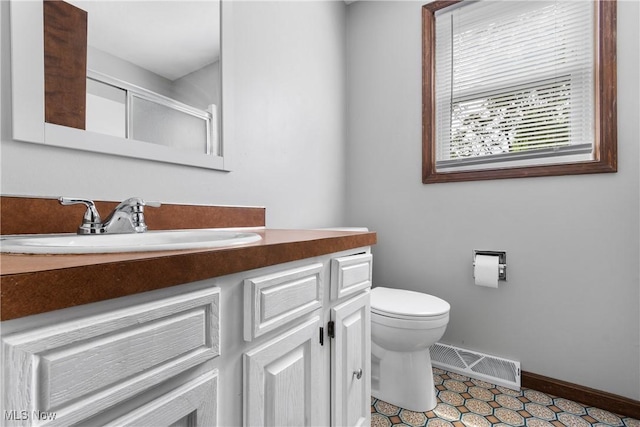 bathroom with toilet, a shower stall, vanity, and baseboards