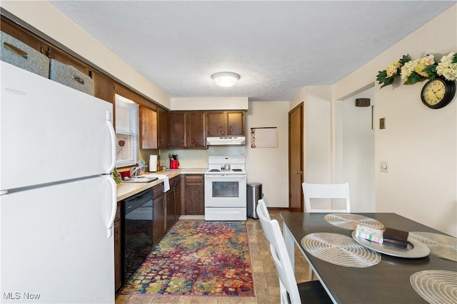 kitchen with white appliances, under cabinet range hood, light countertops, a textured ceiling, and a sink
