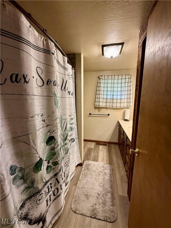 6141 Avon Rd NE, Carrollton, OH 44615 - bathroom with wood finished floors, vanity, a textured ceiling, baseboards, and a shower with curtain