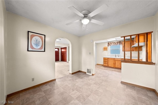 2021 17th St NE, Canton, OH 44705 - unfurnished room featuring baseboards, arched walkways, a ceiling fan, a sink, and a textured ceiling