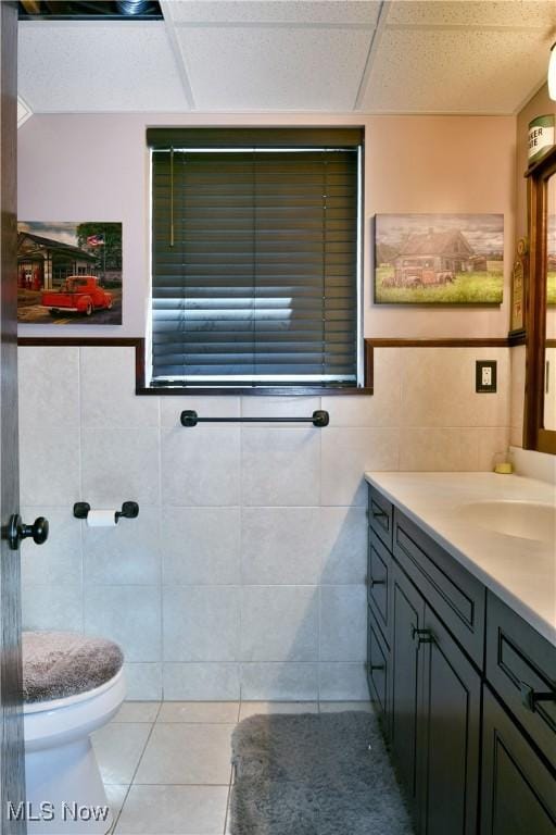 bathroom featuring tile walls, tile patterned floors, vanity, toilet, and a paneled ceiling