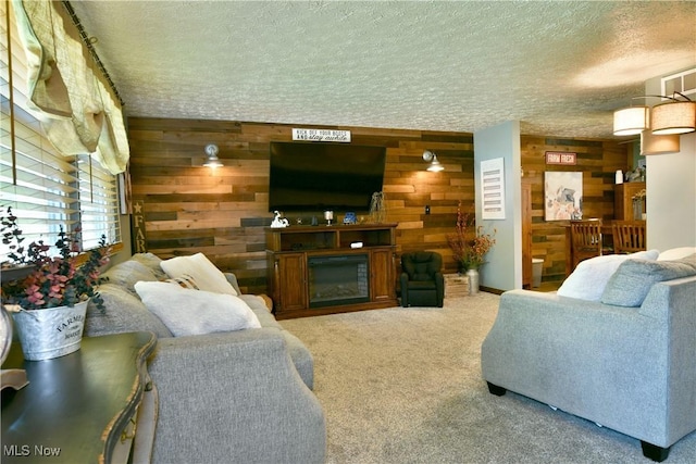 living area featuring wooden walls, a textured ceiling, a glass covered fireplace, and carpet floors