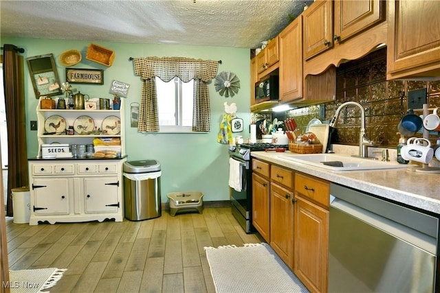 kitchen featuring stainless steel appliances, a sink, light wood-style flooring, a textured ceiling, and light countertops