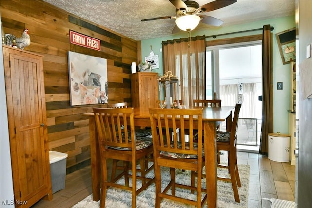 dining area with wood walls, plenty of natural light, ceiling fan, a textured ceiling, and light wood-type flooring
