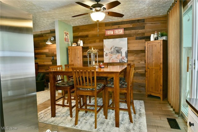 dining room with wooden walls, a textured ceiling, ceiling fan, and light wood-style floors