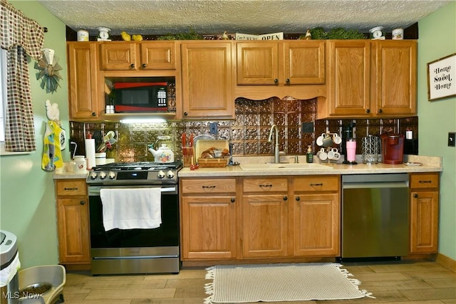 kitchen featuring stainless steel appliances, a sink, light countertops, decorative backsplash, and a textured ceiling