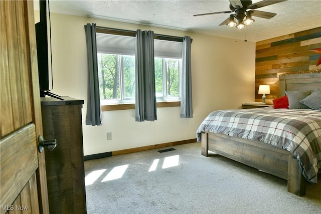 carpeted bedroom with a textured ceiling, baseboards, wood walls, and a ceiling fan