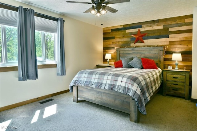 bedroom with carpet flooring, wooden walls, a textured ceiling, baseboards, and a ceiling fan