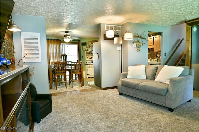 living area featuring carpet flooring, a textured ceiling, ceiling fan, stairs, and baseboards