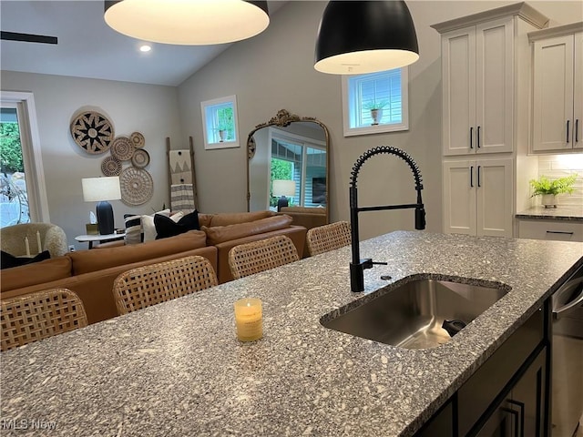 kitchen featuring a sink, open floor plan, vaulted ceiling, dark stone countertops, and dishwasher