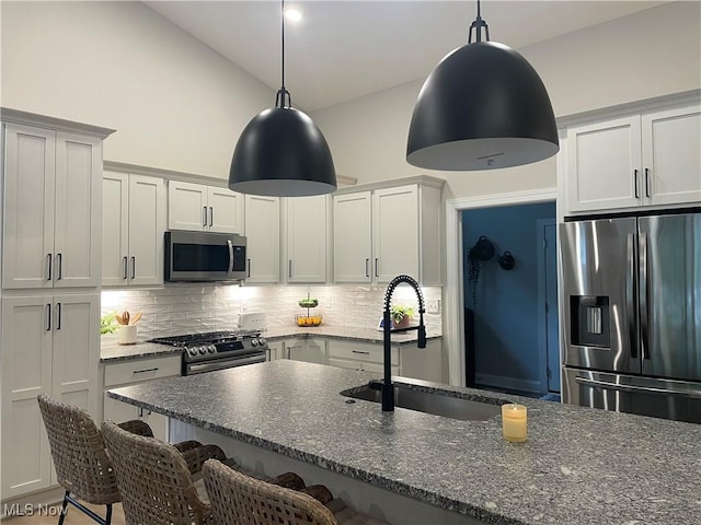 kitchen featuring stainless steel appliances, a sink, a breakfast bar, tasteful backsplash, and dark stone counters
