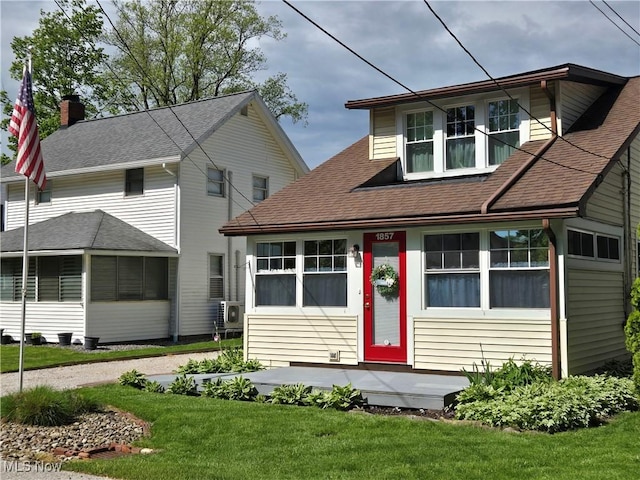 view of front of home featuring a front yard, a sunroom, a shingled roof, a cooling unit, and a chimney