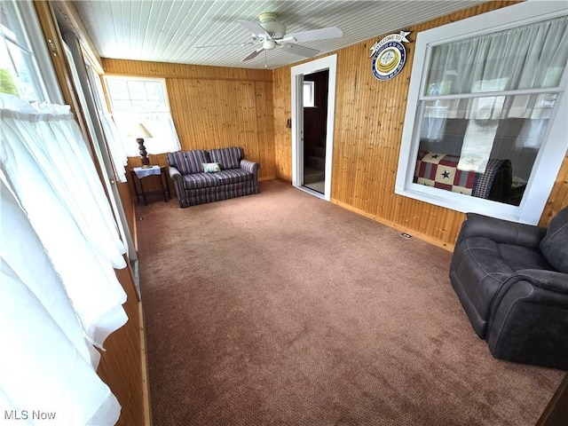 living room featuring carpet floors, a ceiling fan, wood walls, and baseboards