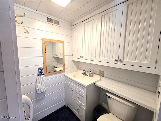 bathroom featuring toilet, vanity, and wooden walls