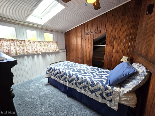 bedroom with carpet, a skylight, ceiling fan, and wooden walls