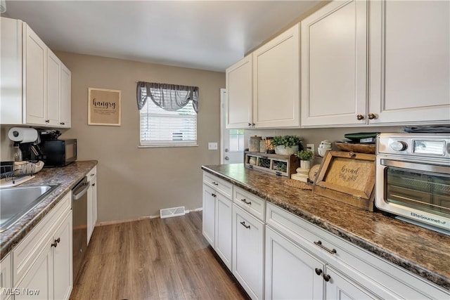 kitchen with wood finished floors, stainless steel dishwasher, white cabinets, baseboards, and black microwave