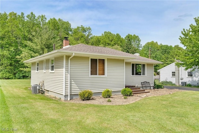 rear view of house featuring a chimney, a yard, cooling unit, and roof with shingles