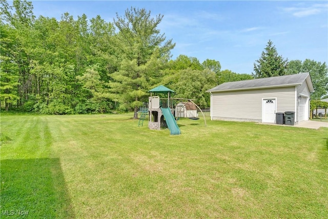 view of green lawn with a playground, an outdoor structure, and a detached garage