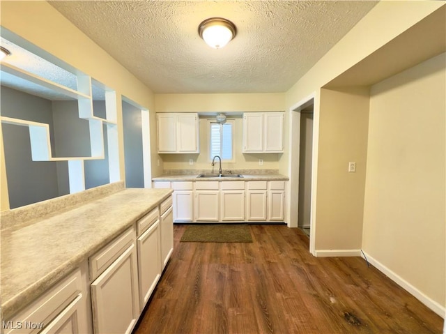 kitchen with a sink, a textured ceiling, dark wood-style flooring, light countertops, and white cabinets