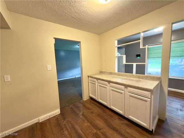kitchen featuring dark wood-style floors, white cabinets, a textured ceiling, light countertops, and baseboards