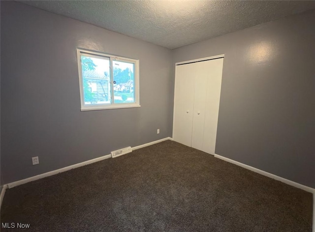 unfurnished bedroom with a textured ceiling, carpet flooring, a closet, and baseboards