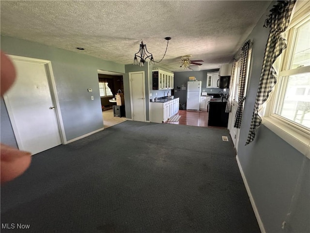 61272 Salem Rd, Salesville, OH 43778 - unfurnished living room featuring a ceiling fan, baseboards, a textured ceiling, dark colored carpet, and a chandelier