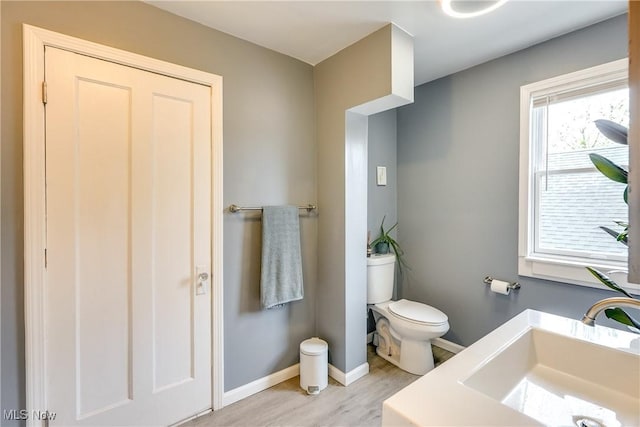 bathroom with a sink, toilet, wood finished floors, and baseboards