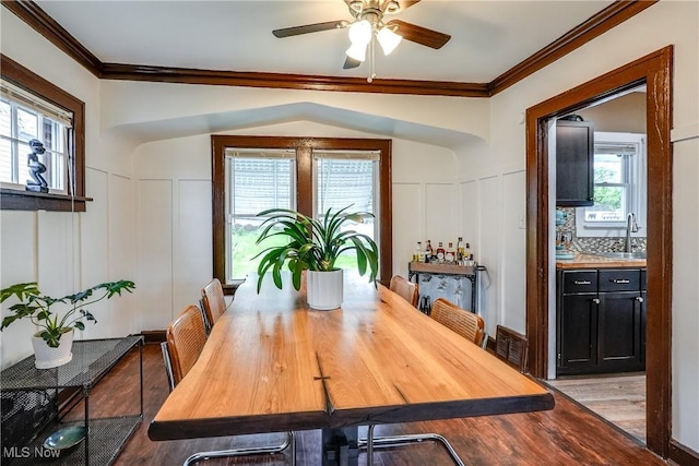dining area with a decorative wall, light wood-style flooring, a ceiling fan, crown molding, and healthy amount of natural light