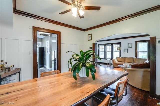 dining area with a decorative wall, ceiling fan, dark wood finished floors, wainscoting, and arched walkways