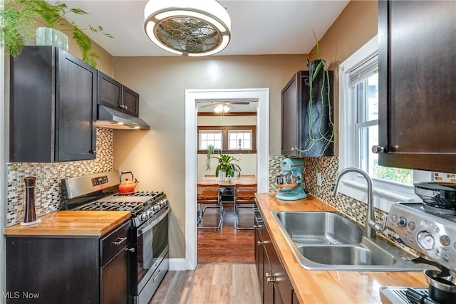 kitchen featuring butcher block countertops, stainless steel gas stove, under cabinet range hood, and a sink