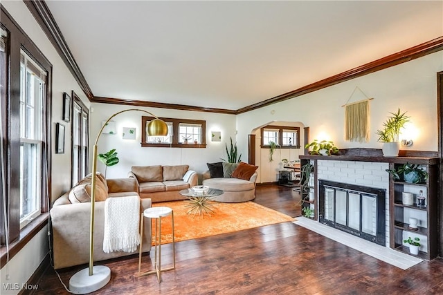 living room featuring wood finished floors, crown molding, a brick fireplace, and arched walkways