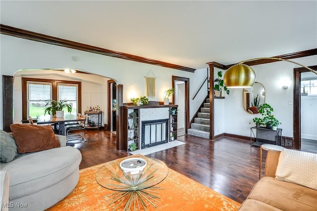 living room with crown molding, arched walkways, wood finished floors, a fireplace, and baseboards