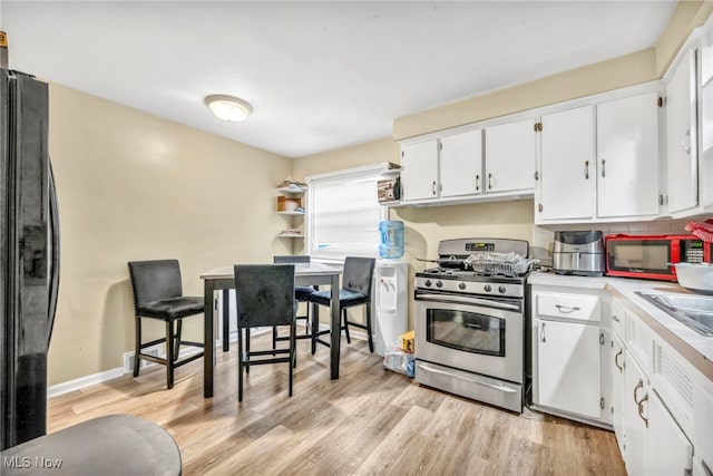 21407 Libby Rd, Maple Heights, OH 44137 - kitchen featuring stainless steel gas range oven, freestanding refrigerator, white cabinets, light wood-style flooring, and light countertops