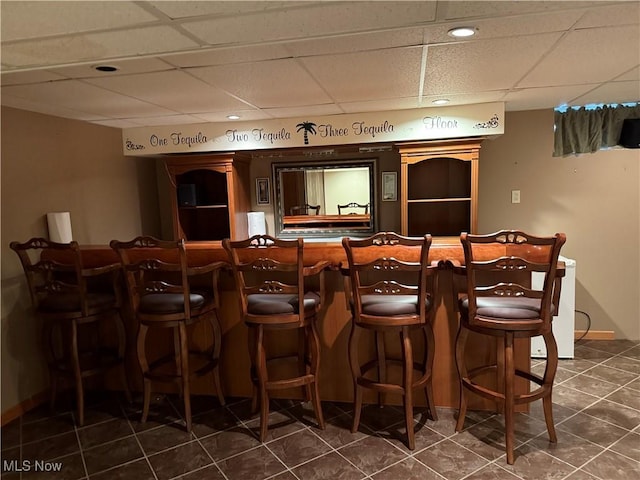 indoor dry bar with a drop ceiling, dark tile patterned floors, and recessed lighting