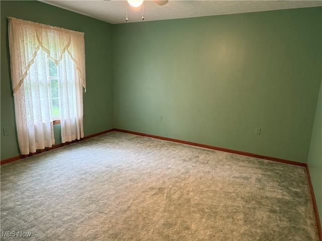 carpeted spare room with a ceiling fan and baseboards