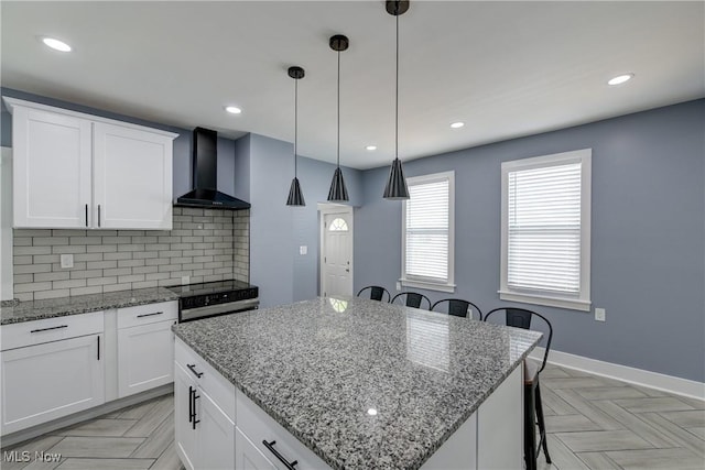 kitchen with wall chimney exhaust hood, range with electric cooktop, a breakfast bar, decorative backsplash, and a center island