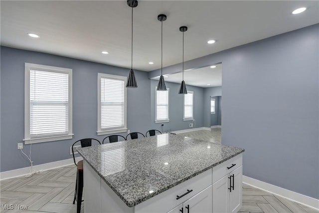 kitchen with a center island, a breakfast bar area, white cabinets, hanging light fixtures, and light stone countertops