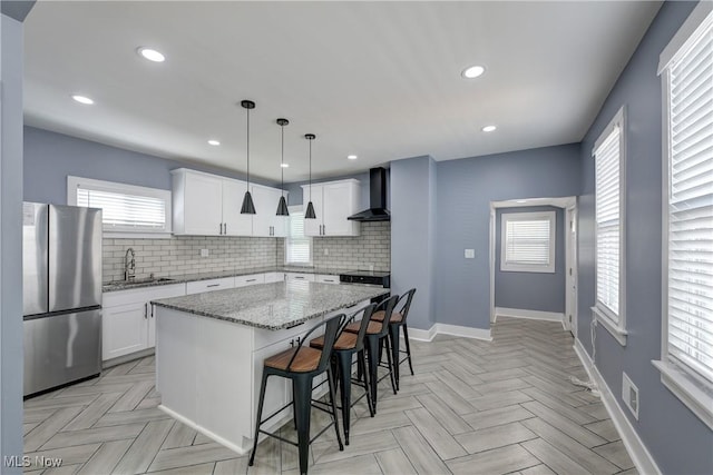kitchen with freestanding refrigerator, wall chimney exhaust hood, a sink, a kitchen island, and decorative backsplash