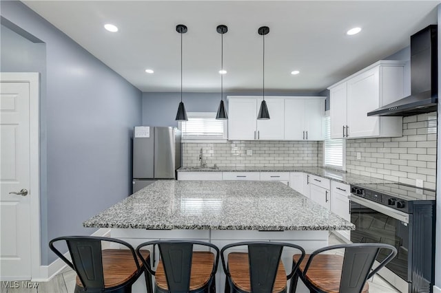 kitchen with wall chimney range hood, freestanding refrigerator, a sink, tasteful backsplash, and recessed lighting