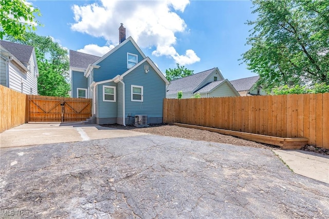 rear view of property featuring cooling unit, a chimney, a fenced backyard, and asphalt driveway
