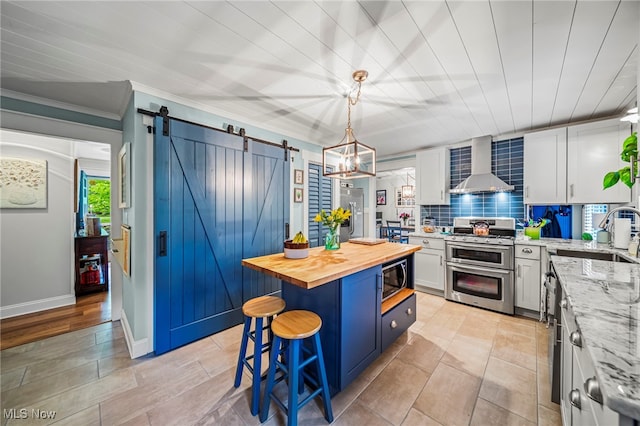 kitchen with appliances with stainless steel finishes, wall chimney range hood, a sink, wooden counters, and a barn door