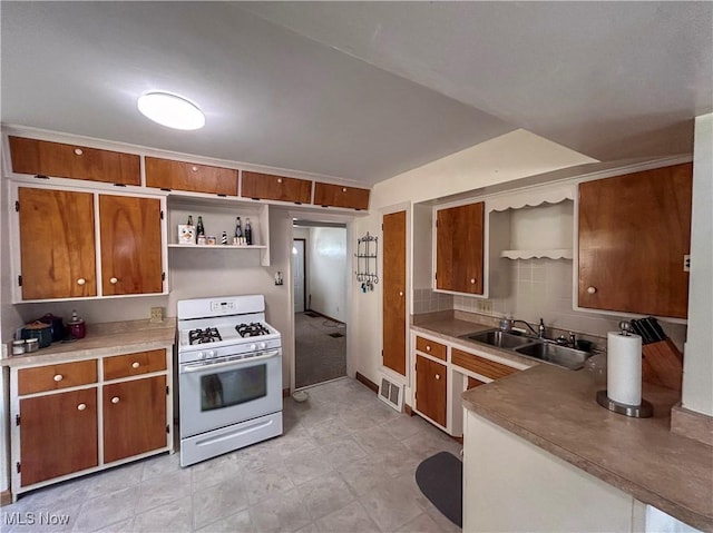 kitchen with white range with gas cooktop, a sink, open shelves, brown cabinets, and decorative backsplash