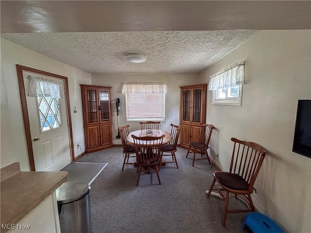 carpeted dining area with a textured ceiling and baseboards