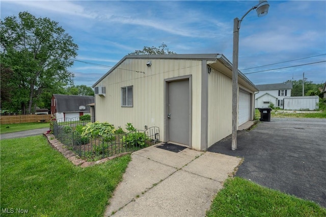 390 E Clark St, East Palestine, OH 44413 - view of outdoor structure featuring fence, asphalt driveway, a wall mounted AC, and an outbuilding