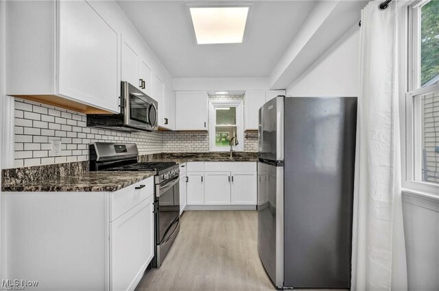 1212 Eastwood Ave, Mayfield Heights, OH 44124 - kitchen with stainless steel appliances, light wood-style floors, white cabinetry, backsplash, and dark stone counters