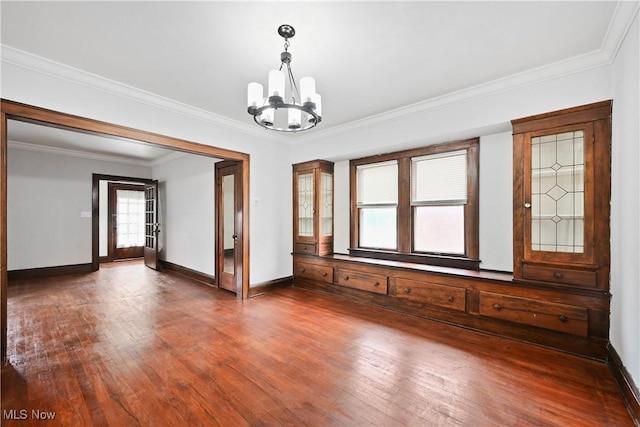 empty room featuring a chandelier, wood finished floors, baseboards, crown molding, and french doors