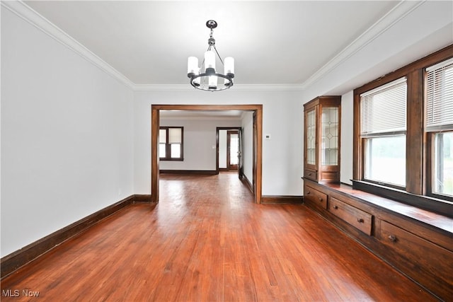 empty room featuring a chandelier, baseboards, wood finished floors, and crown molding