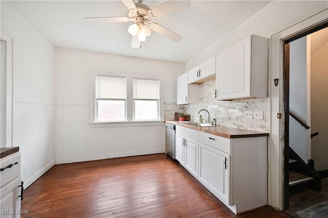 kitchen featuring a sink, stainless steel dishwasher, dark wood finished floors, white cabinetry, and wainscoting