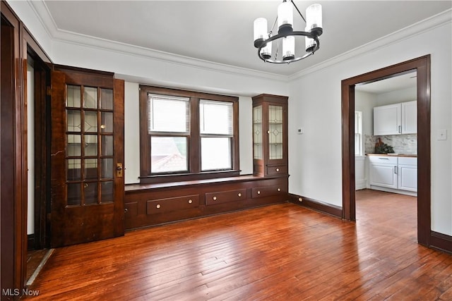 spare room featuring a chandelier, hardwood / wood-style floors, ornamental molding, and baseboards