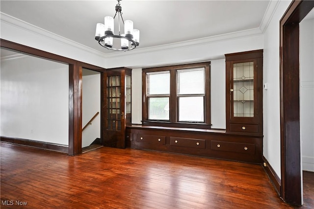 spare room featuring a chandelier, hardwood / wood-style floors, ornamental molding, and baseboards